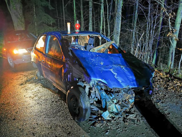 Porzucony wrak auta, a na nim palące się znicze