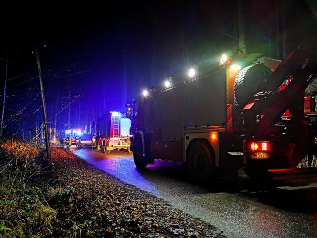 Porzucony wrak auta, a na nim palące się znicze